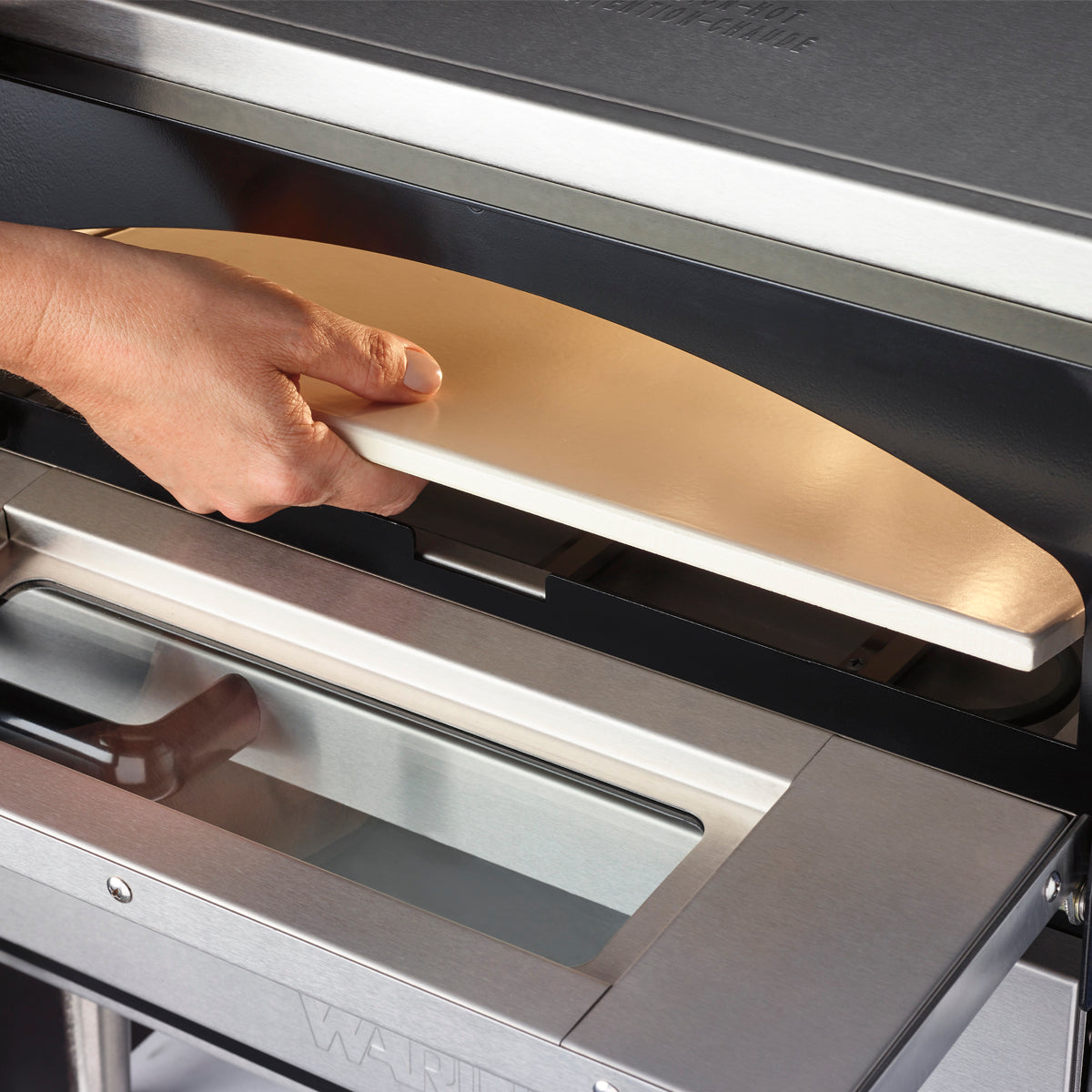 Hand sliding the ceramic deck out of a Waring WPO350 pizza oven, close-up